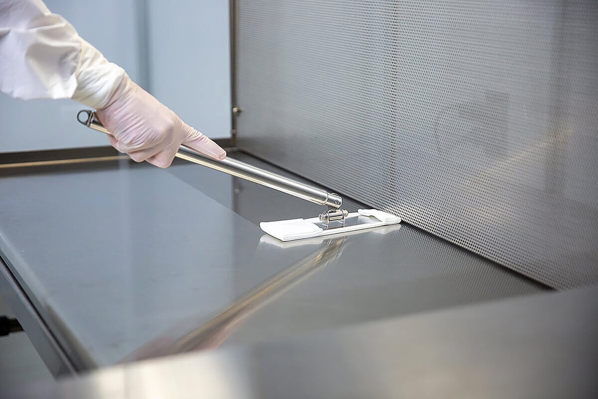 EasyReach isolator mop tool being used to wipe a stainless steel cleanroom work surface with a bound-edge poly mop pad attached.